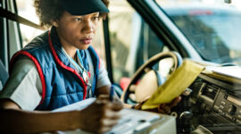 Female driver sitting inside a delivery van reviewing documents and taking notes during commercial driver training.